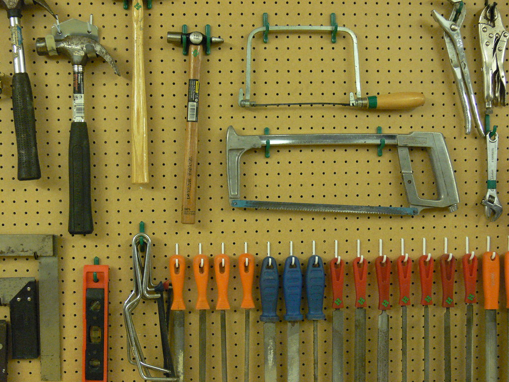 Outils à main soigneusement rangés sur un panneau perforé : scies, marteaux, limes et pinces